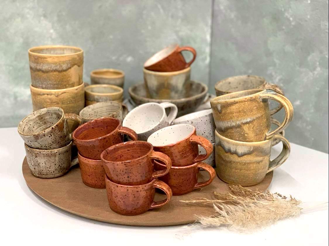 Verschiedene handgefertigte Keramiktassen in Braun, Beige und Weiß stehen auf einem Holztablett.